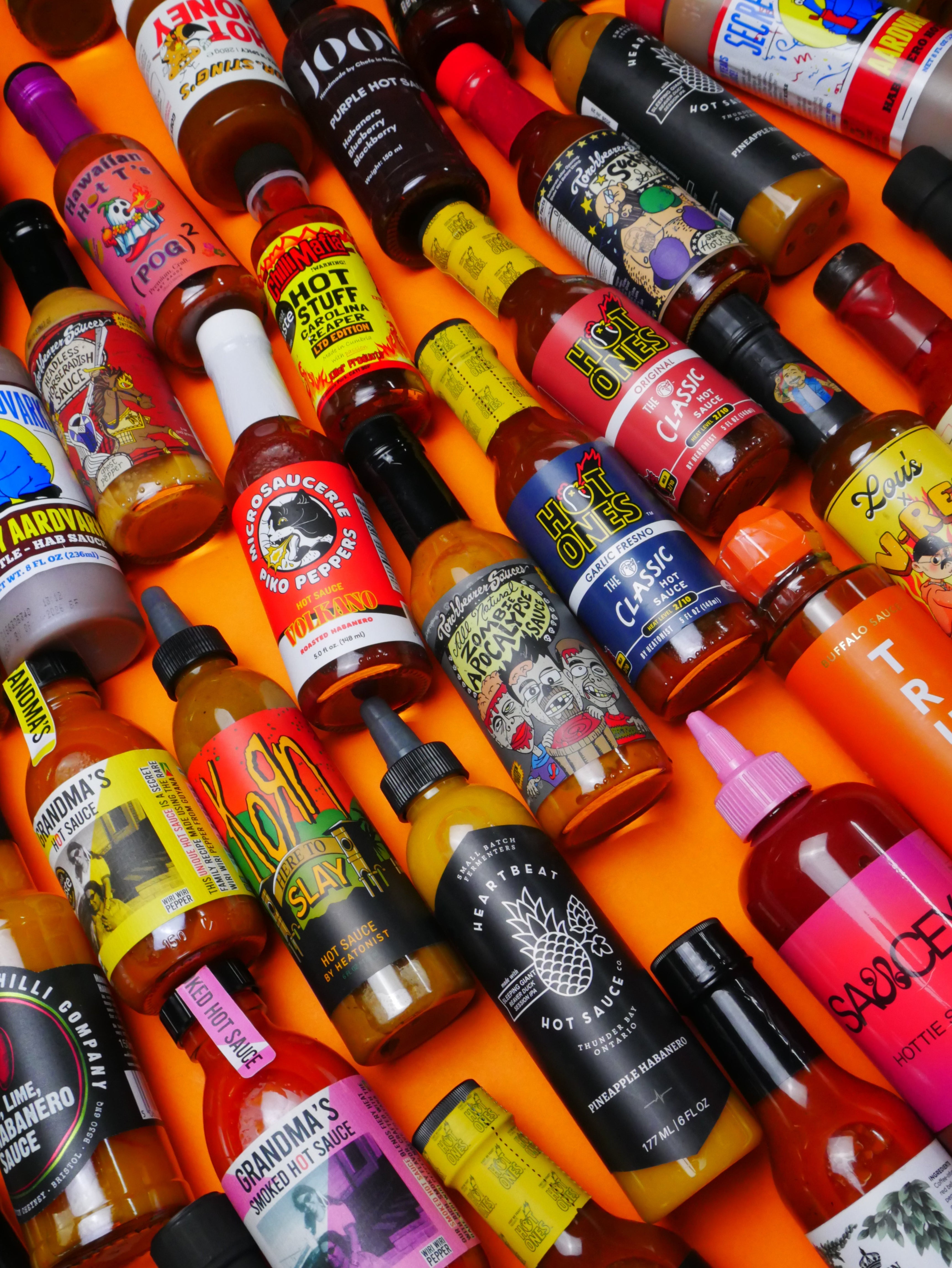 Collection of various hot sauce bottles with colorful labels on an orange background